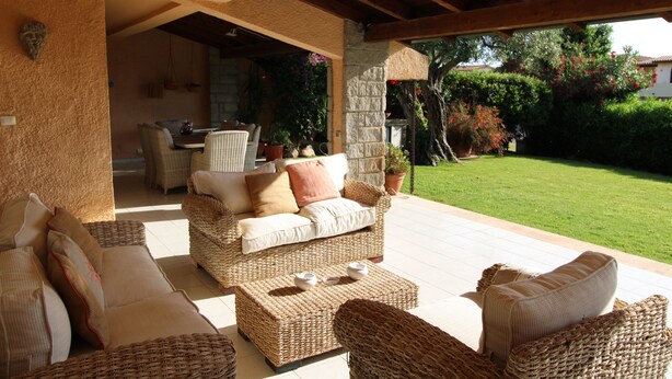 Une terrasse extérieure aménagée avec des meubles en osier, des piliers en pierre et une vue sur un jardin.