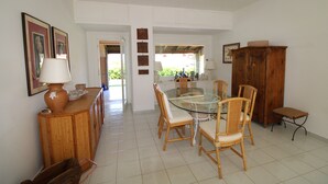 Un coin repas avec une table en verre entourée de chaises en osier, un buffet en bois et un banc.