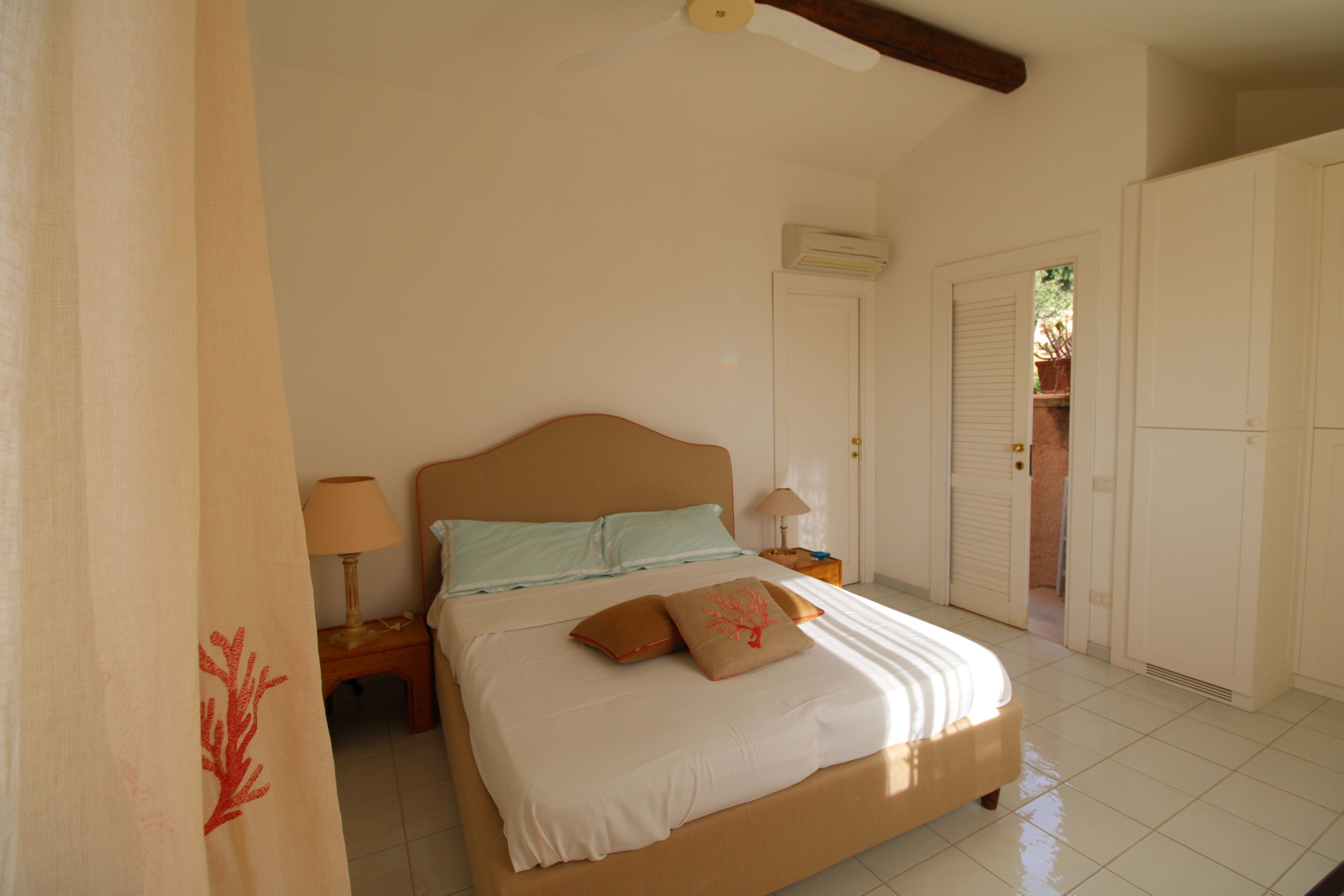 Une chambre à coucher comprenant un lit, des tables de chevet, un ventilateur de plafond, un appareil de climatisation et une armoire.