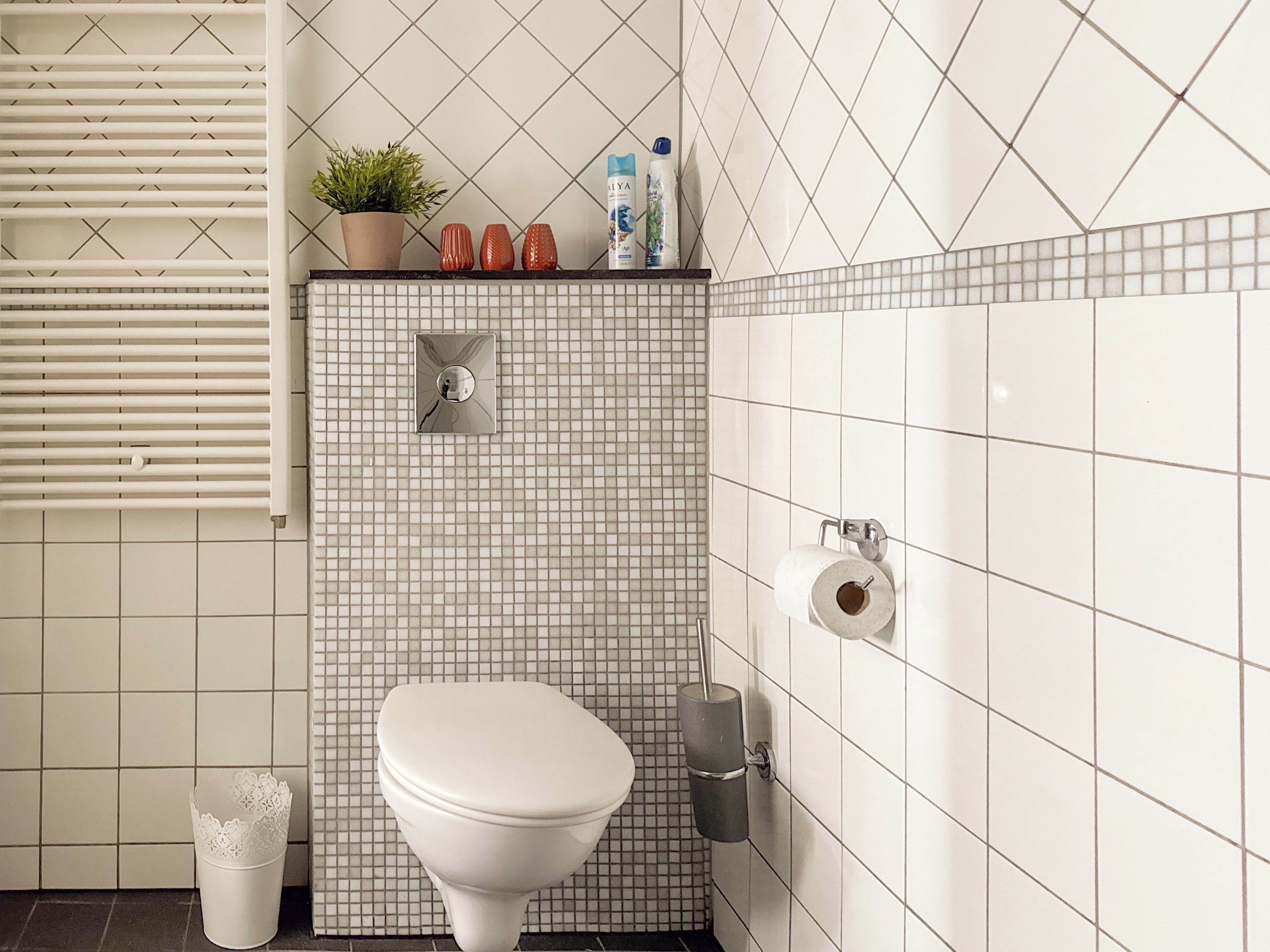 A bathroom with a toilet, a hand dryer, a paper towel dispenser, and a potted plant on the wall.