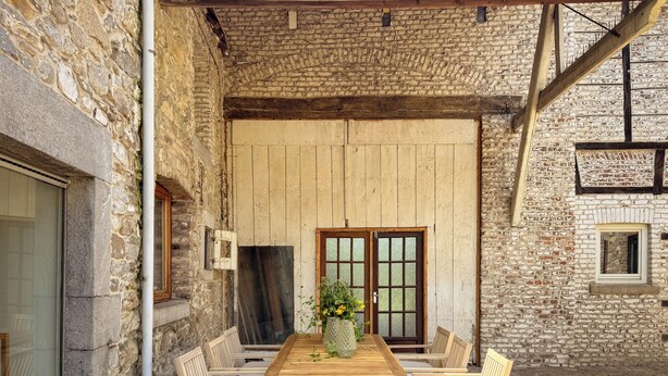 Una mesa de madera al aire libre con sillas, una planta en maceta y un muro de ladrillo.
