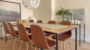 Un comedor con una mesa de madera, sillas marrones, una cesta tejida, una lámpara colgante y cuadros en las paredes.