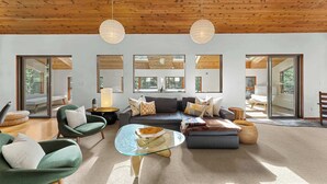Ein geräumiges Wohnzimmer mit Holzboden, großen Fenstern und einer modernen Sofagarnitur.