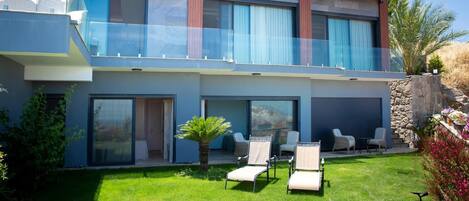 Une maison moderne à deux étages, dotée d’un balcon, d’une terrasse avec des chaises et d’une pelouse bien entretenue.
