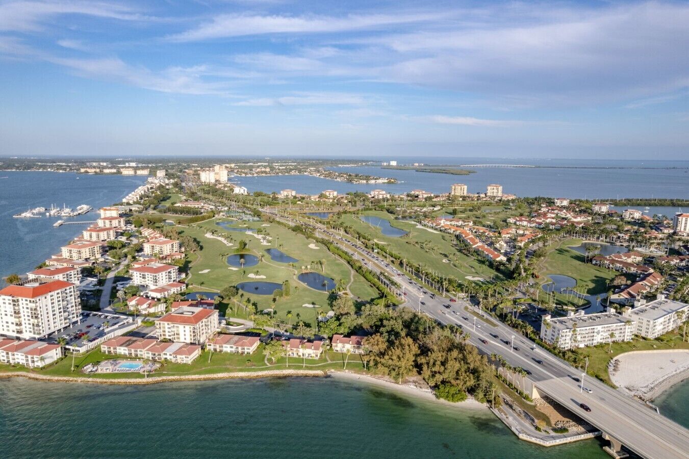 An aerial view of a coastal resort area with multiple buildings, a golf course, and a bridge connecting to the mainland.