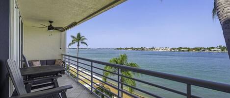 Un balcón con vista al mar, un ventilador de techo y una mesa con sillas.