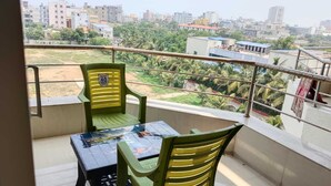 A balcony with two green chairs and a table, overlooking a residential area with buildings and greenery.