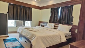 A hotel room with a bed, a bedside table, a window with curtains, and an air conditioning unit.