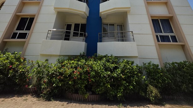 A high-rise building with multiple balconies, a central blue feature, and surrounding greenery.