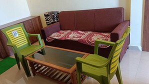 A living room with a sofa, two green chairs, a glass coffee table, and a zebra-patterned throw.