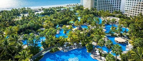 A resort with multiple swimming pools surrounded by palm trees and a view of the ocean.