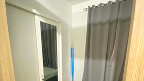Ein schmaler Flur mit einer Tür zu einem Zimmer, das ein Bett und einen Vorhang hat.