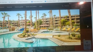 A resort with a swimming pool, palm trees, and a building with balconies.