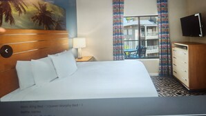 A hotel room with a king bed, a wooden headboard, a TV mounted on the wall, a window with curtains, and a view of the outside.