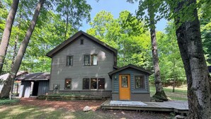 A two-story house with a small attached garage, surrounded by trees.