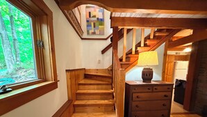 A wooden staircase leading to a kitchen area with a washing machine and a lamp on a nightstand.