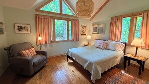 A bedroom with a large bed, a chair, two bedside tables, and a window with curtains.