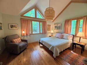 Een slaapkamer met een groot bed, een stoel, twee nachtkastjes en een raam met gordijnen.