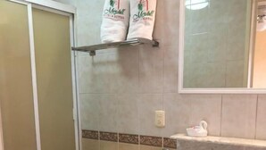 A bathroom with a toilet, sink, and shower. There are towels on a shelf above the sink. - HOTEL MEZVALL (Morelia)