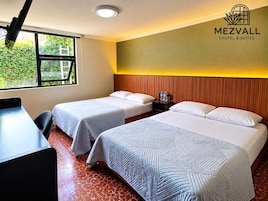 Habitación de hotel con dos camas, un escritorio y una ventana con vistas a zonas verdes.