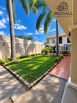 Un patio bien cuidado con césped impecable, palmeras y un área de patio con mobiliario exterior.