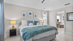 A bedroom with a bed, two bedside tables with lamps, a ceiling fan, and framed artwork on the wall. - Fire Pit Pool Retreat for Groups (Kissimmee)
