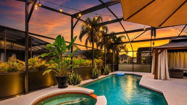 A rooftop pool with a hot tub, surrounded by plants and a sunset view. - Fire Pit Pool Retreat for Groups (Kissimmee)