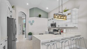 A modern kitchen with a large island, stainless steel appliances, and bar stools. - Fire Pit Pool Retreat for Groups (Kissimmee)