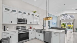 A modern kitchen with white cabinets, stainless steel appliances, and a pendant light. - Fire Pit Pool Retreat for Groups (Kissimmee)