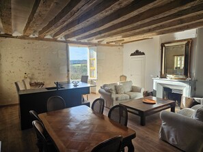 Ein rustikales Interieur mit sichtbaren Holzbalken, einem Essbereich, einer Couch und einem Kamin.
