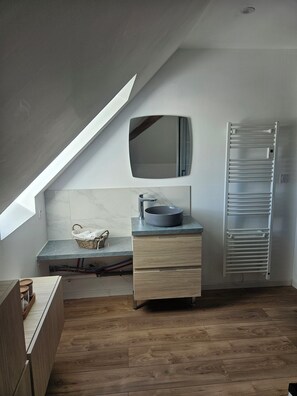 Ein modernes Badezimmer mit Dachfenster, einem runden Waschbecken, einem Spiegel und einem Handtuchhalter.