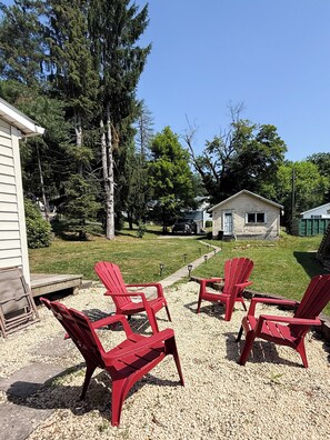 A backyard with red Adirondack chairs, a gravel path, and a small house with a garage.