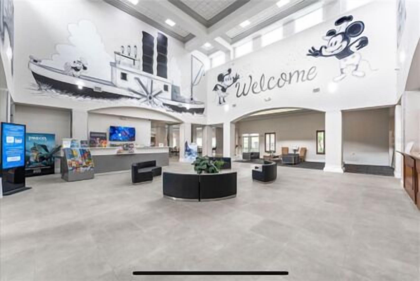 Un hall d’entrée spacieux, agrémenté d’une pancarte « Bienvenue », d’un comptoir d’accueil, de coins salon et d’un grand écran numérique.