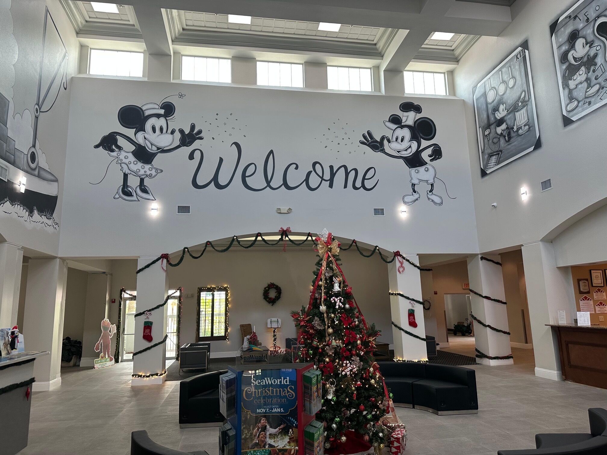 A lobby with a large 'Welcome' sign, a decorated Christmas tree, and Mickey Mouse murals.