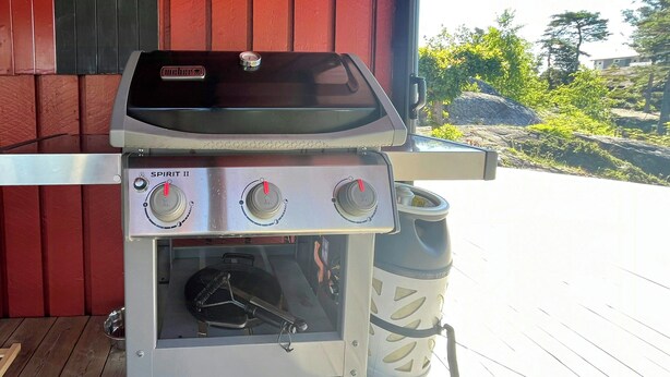 A portable gas grill with two control knobs and a vented cooking area, placed on a wooden deck.