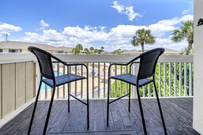 A wooden deck with two chairs, a pool, and a view of a residential area with palm trees. - Pool & Golf Course Views at Sandpiper Cove Unit 2014, Beach in Destin, FL (Destin)