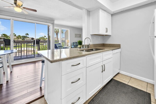A kitchen with white cabinets, a granite countertop, a built-in sink, and a ceiling fan. - Pool & Golf Course Views at Sandpiper Cove Unit 2014, Beach in Destin, FL (Destin)