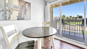 Ein Zimmer mit einem runden Tisch und zwei Stühlen, eine Schiebetür zu einem Balkon mit Gartenmöbeln.
