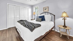 Ein Schlafzimmer mit einem Bett, Nachttischlampen, einem kleinen Tisch und einem Fenster mit Jalousien.