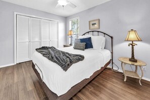 A bedroom with a bed, bedside lamps, a small table, and a window with blinds. - Pool & Golf Course Views at Sandpiper Cove Unit 2014, Beach in Destin, FL (Destin)