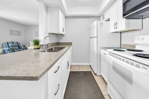 A modern kitchen with white cabinets, a granite countertop, a stainless steel sink, a built-in oven, and a microwave. - Pool & Golf Course Views at Sandpiper Cove Unit 2014, Beach in Destin, FL (Destin)