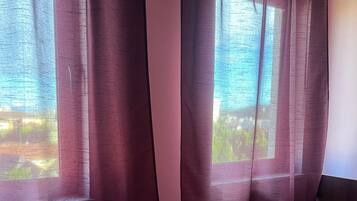 Un dormitorio con una cama, dos ventanas con cortinas y vistas al exterior.