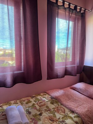 A bedroom with a bed, two windows with curtains, and a view of greenery outside. - REZIDENCA 4R (Shkoder)