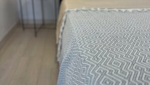 A bed with a patterned blanket, a bedside table with a candle, and a wooden floor.