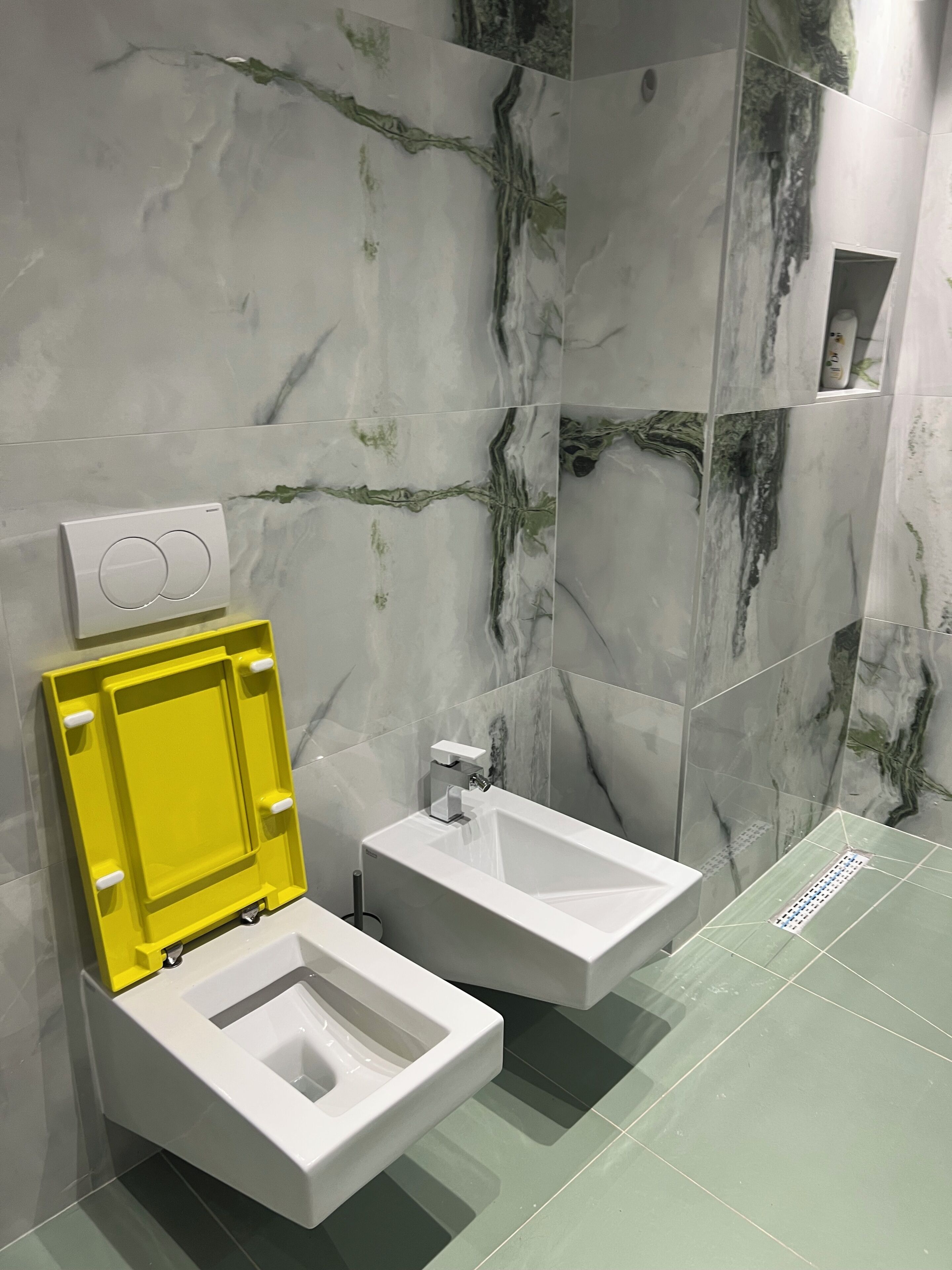 A modern bathroom with a toilet, bidet, and a wall-mounted soap dispenser.