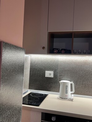 A kitchen with a black induction cooktop, a white electric kettle, and a cabinet with a textured backsplash. - REZIDENCA 4R (Shkoder)