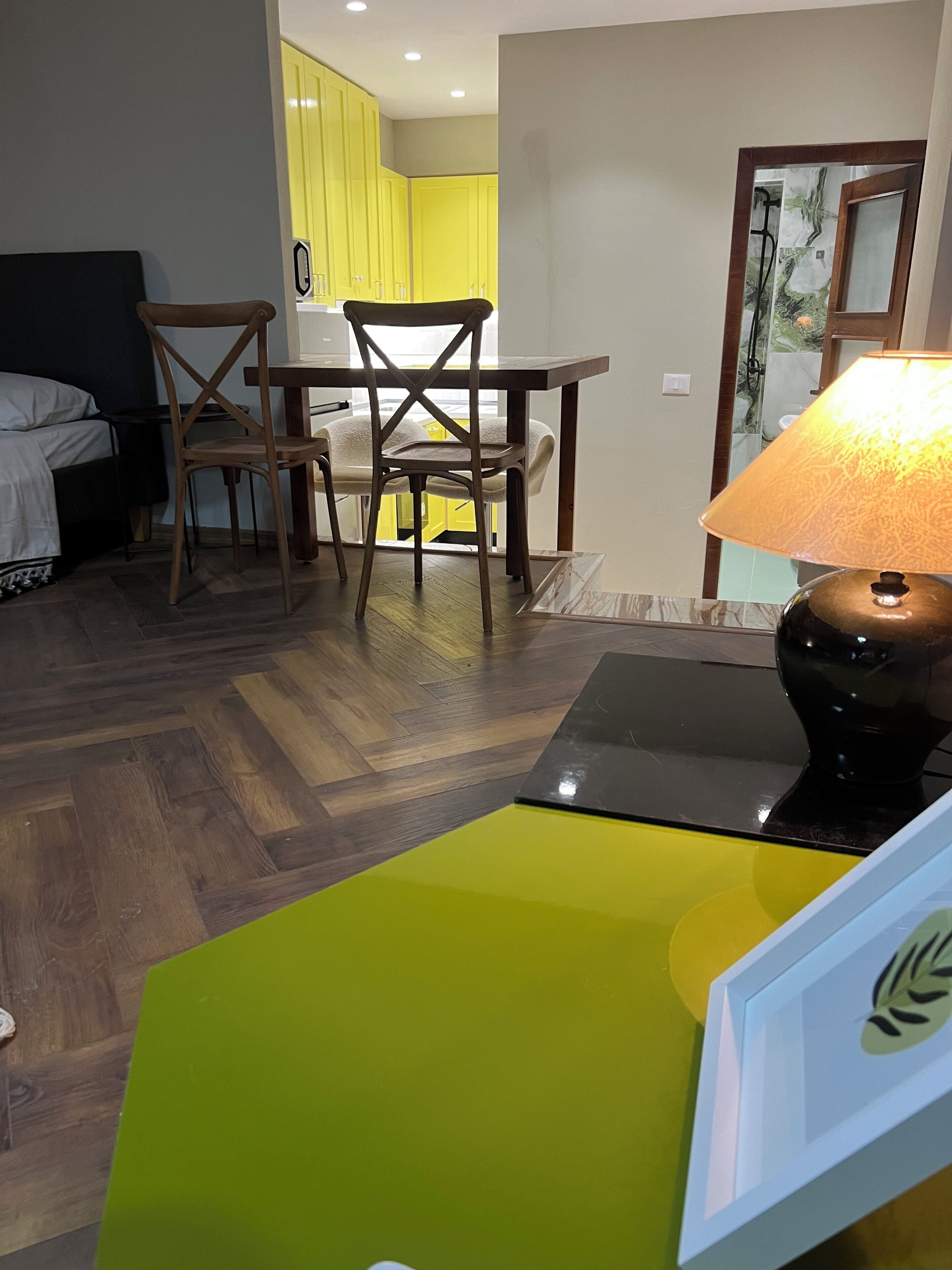 A room with a dining table, chairs, a lamp, and a bed.