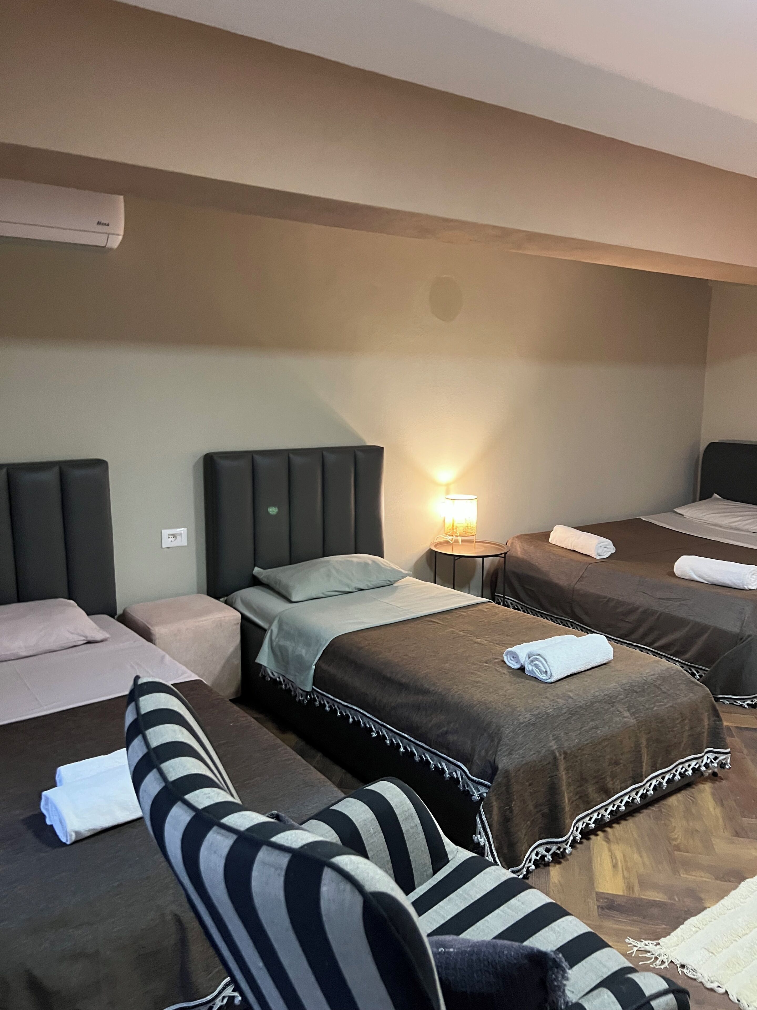 Habitación de hotel con dos camas, una mesita, una silla y aire acondicionado de pared.