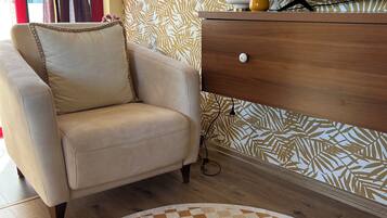 A living room with a sofa, a patterned wall, a TV, and a lamp on a wooden dresser.