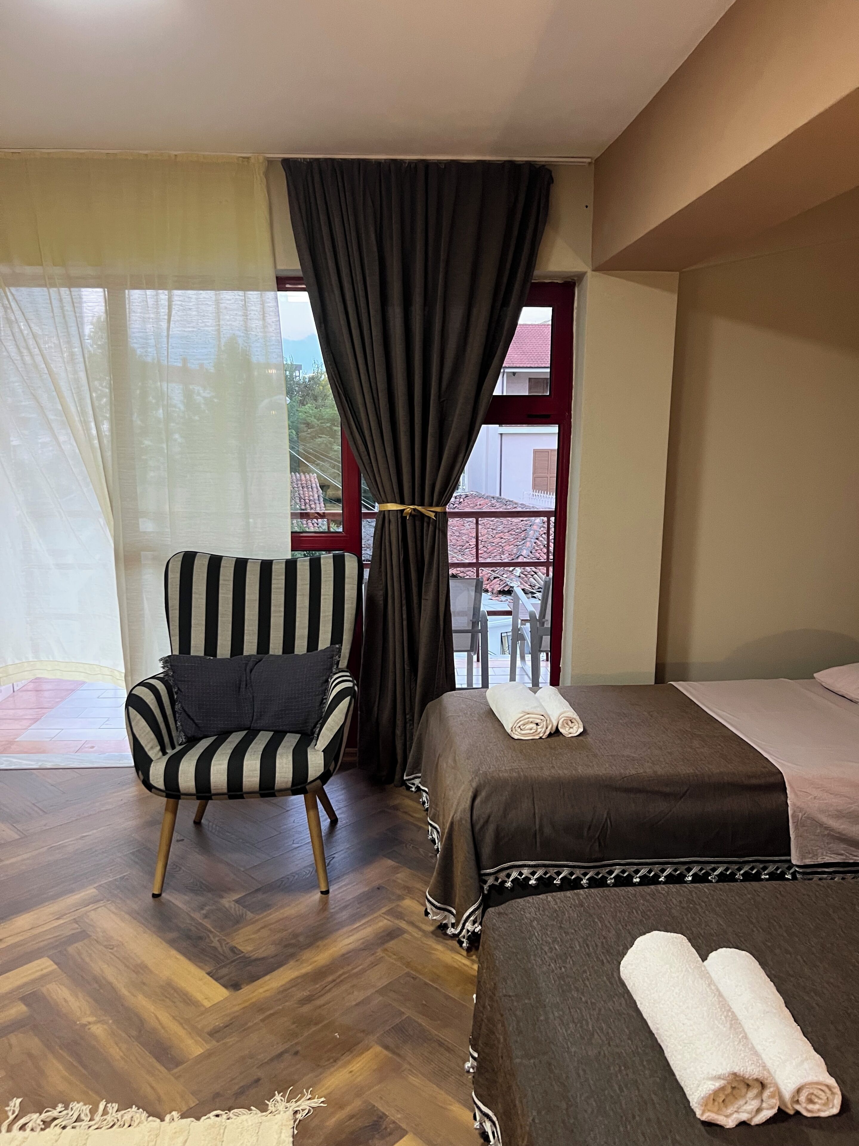 A hotel room with a bed, a striped armchair, a window with curtains, and a view of the outside.